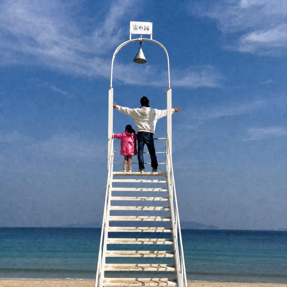 An adult and child posing atop the white "Stairway to the Sky" photo installation on the beach in Itoshima, Fukuoka Prefecture, Japan.